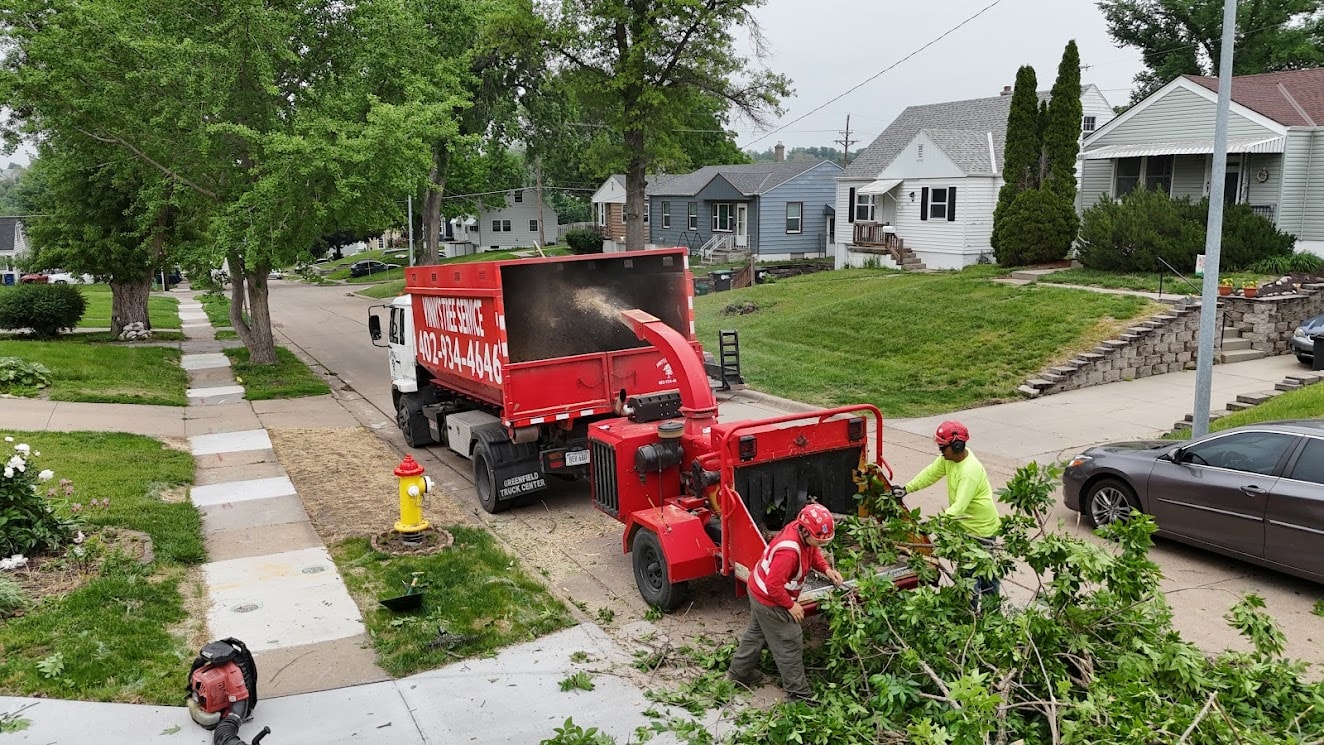 Vinny's Tree Service branded dump truck and chipper with crew chipping branches on residential street in Omaha